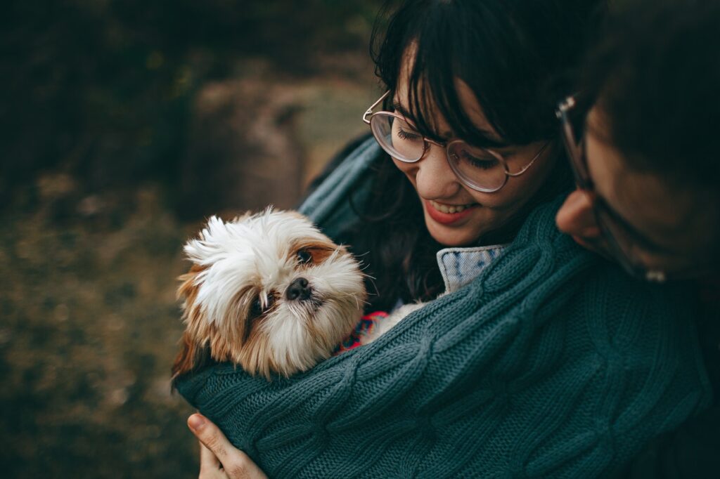 A woman holding a small dog in her arms with the help of a scarf.