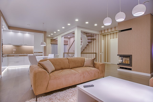 A brightly lit living room and kitchen area with a beige couch as the centerpiece.