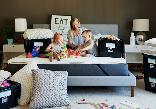 A woman and children sitting on a bed and unpacking boxes