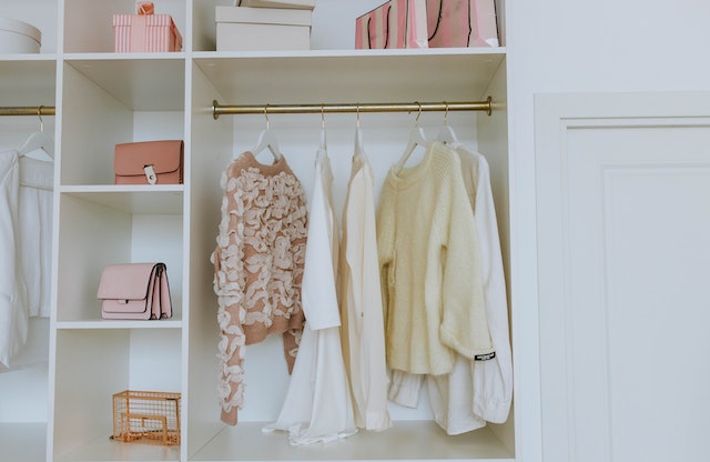 A white closet with pink purses and white shirts and blouses.